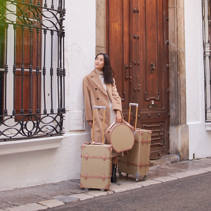 Lifestyle image of model with The Alchemist vegan leather suitcases in  gold