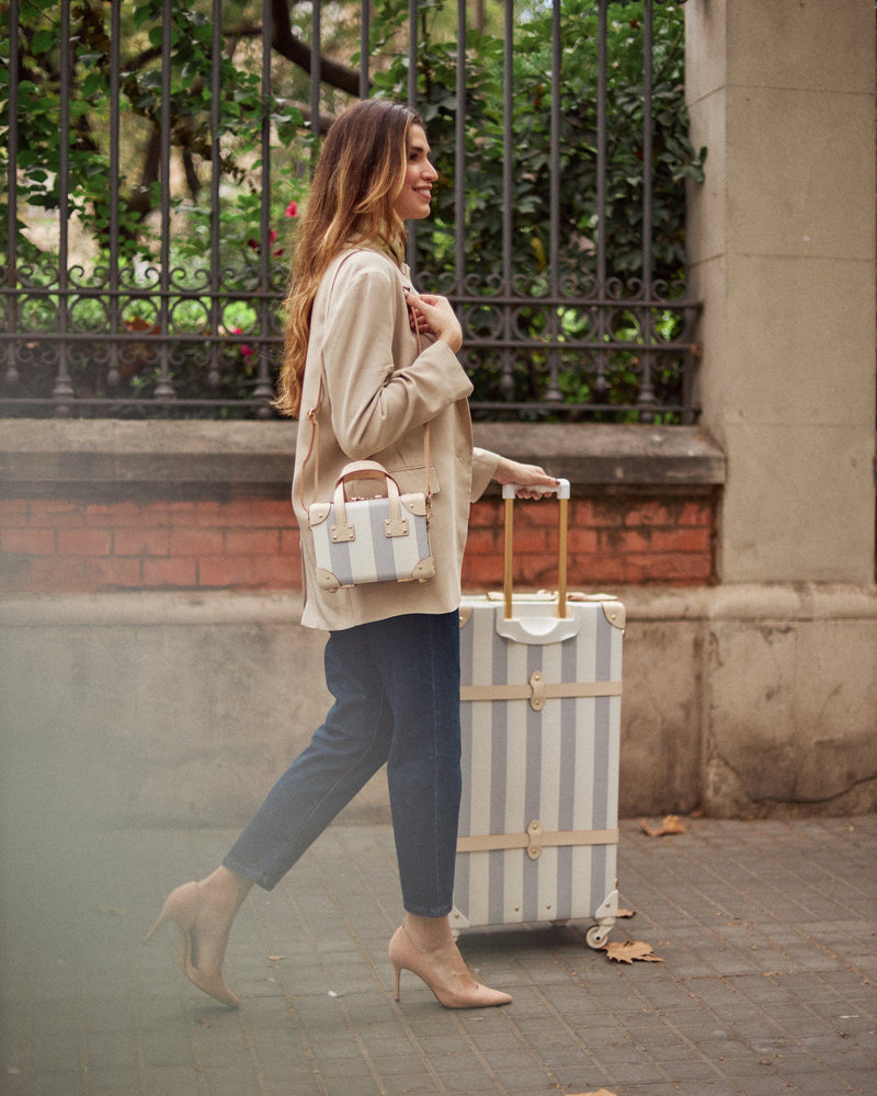 Lifestyle image of model with The Illustrator fibreboard suitcases in blue-stripe