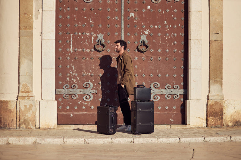 Lifestyle image of male model with The Industrialist fibreboard suitcases in  black 