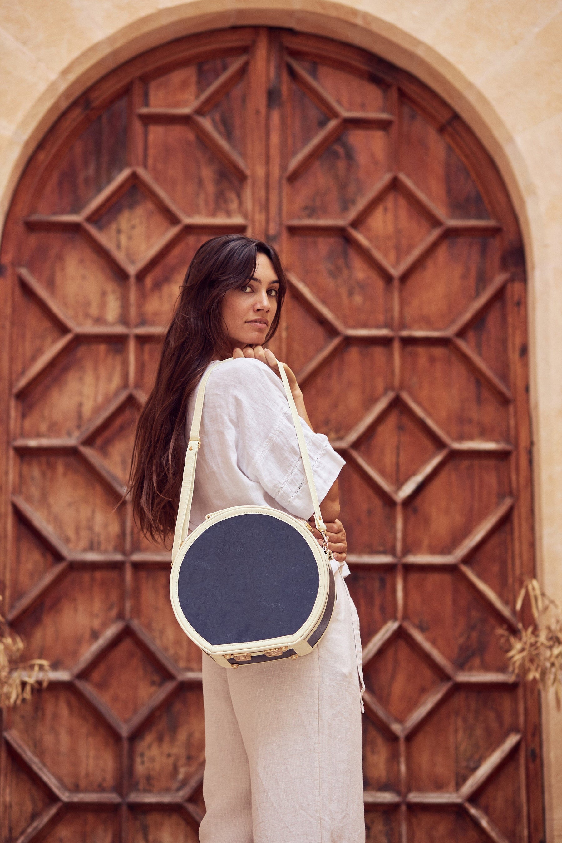 Lifestyle model with the small hatbox Entrepreneur vegan leather suitcase in navy with shoulder attachment strap