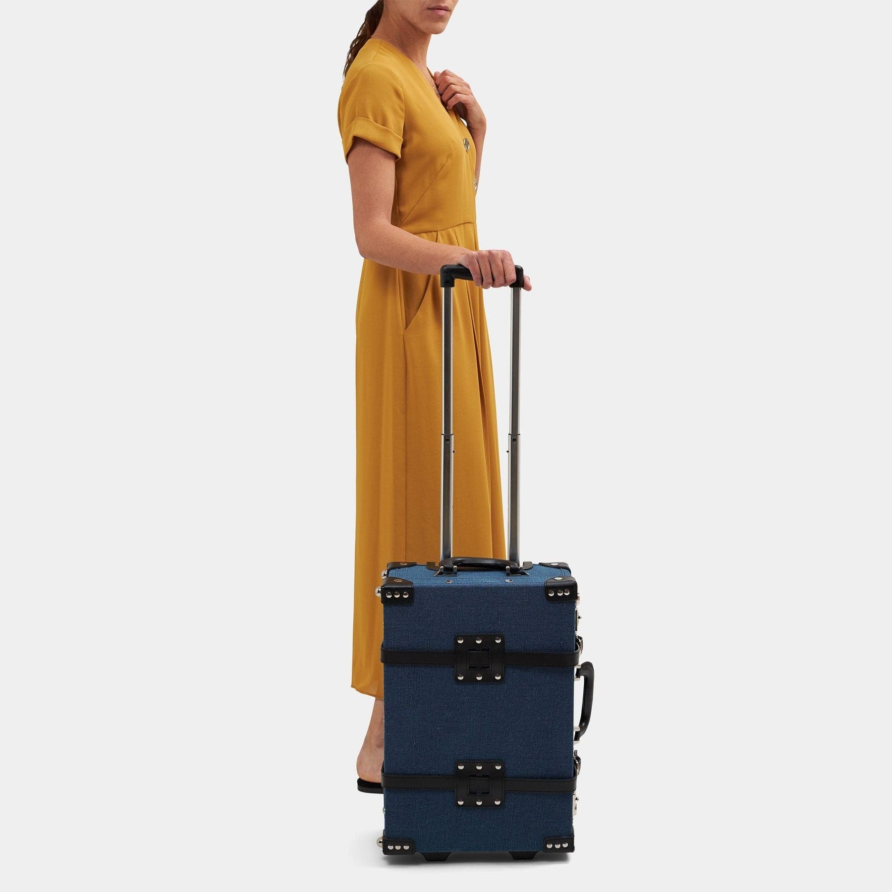 Model with the carry-on Editor linen suitcase with navy body, black trims and raised handle