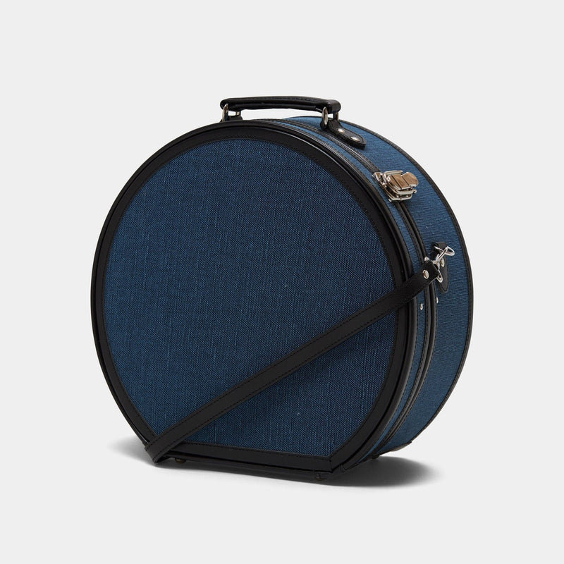 Angled product view of the large hatbox Editor linen suitcase with navy body, black trims and shoulder attachment strap